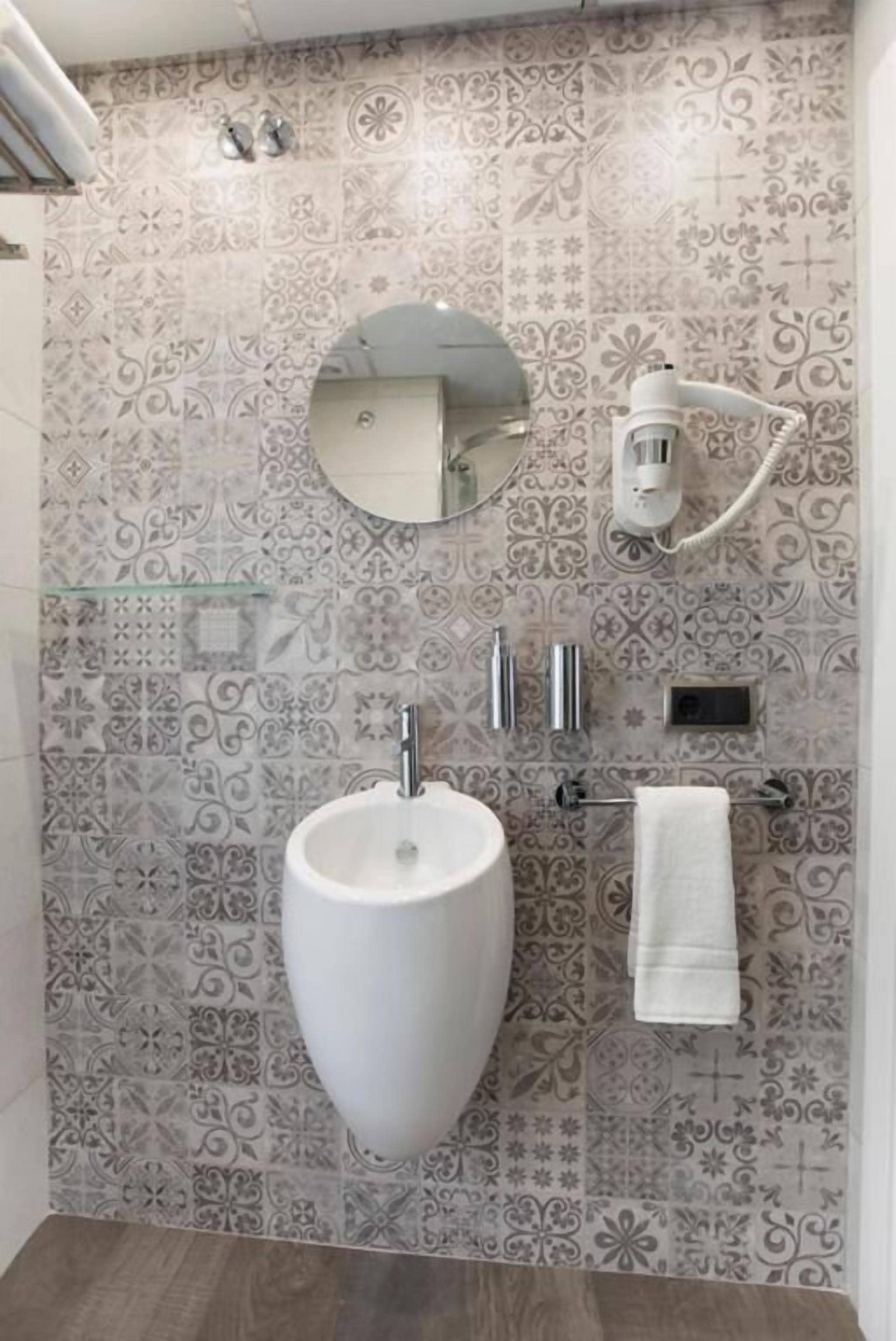 A bathroom with patterned tiles, a white sink, a mirror, a towel rack, and a handheld showerhead.