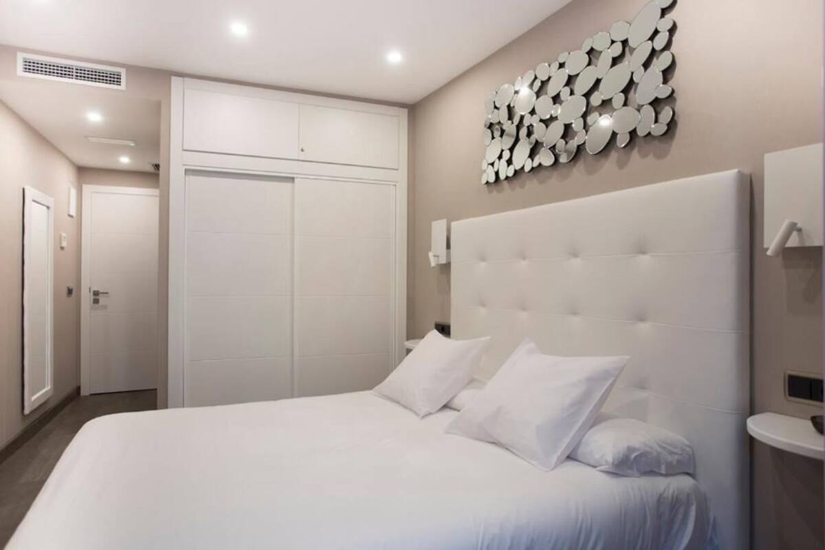 A bedroom with a large bed, a white headboard, a wall-mounted mirror, and a door.