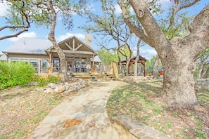 A house with a stone pathway leading to a covered porch, surrounded by large trees and a landscaped garden.