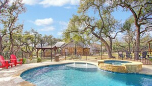 A swimming pool with a fountain, surrounded by trees and red chairs. - Private 14 Acres | Pool, Pickleball, Hot Tub & Guest House with Views (Wimberley)