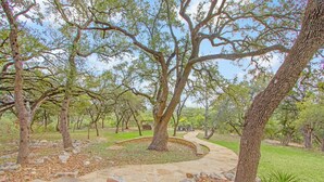 A landscaped garden with stone pathways, trees, and a circular seating area. - Private 14 Acres | Pool, Pickleball, Hot Tub & Guest House with Views (Wimberley)