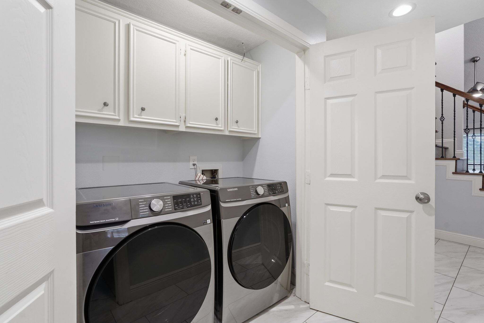 A laundry room with two front-loading washers, white cabinetry, and a white door.