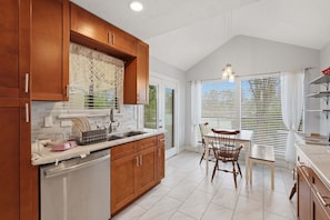 A kitchen with wooden cabinets, a sink, a dining table with chairs, and a window with blinds.