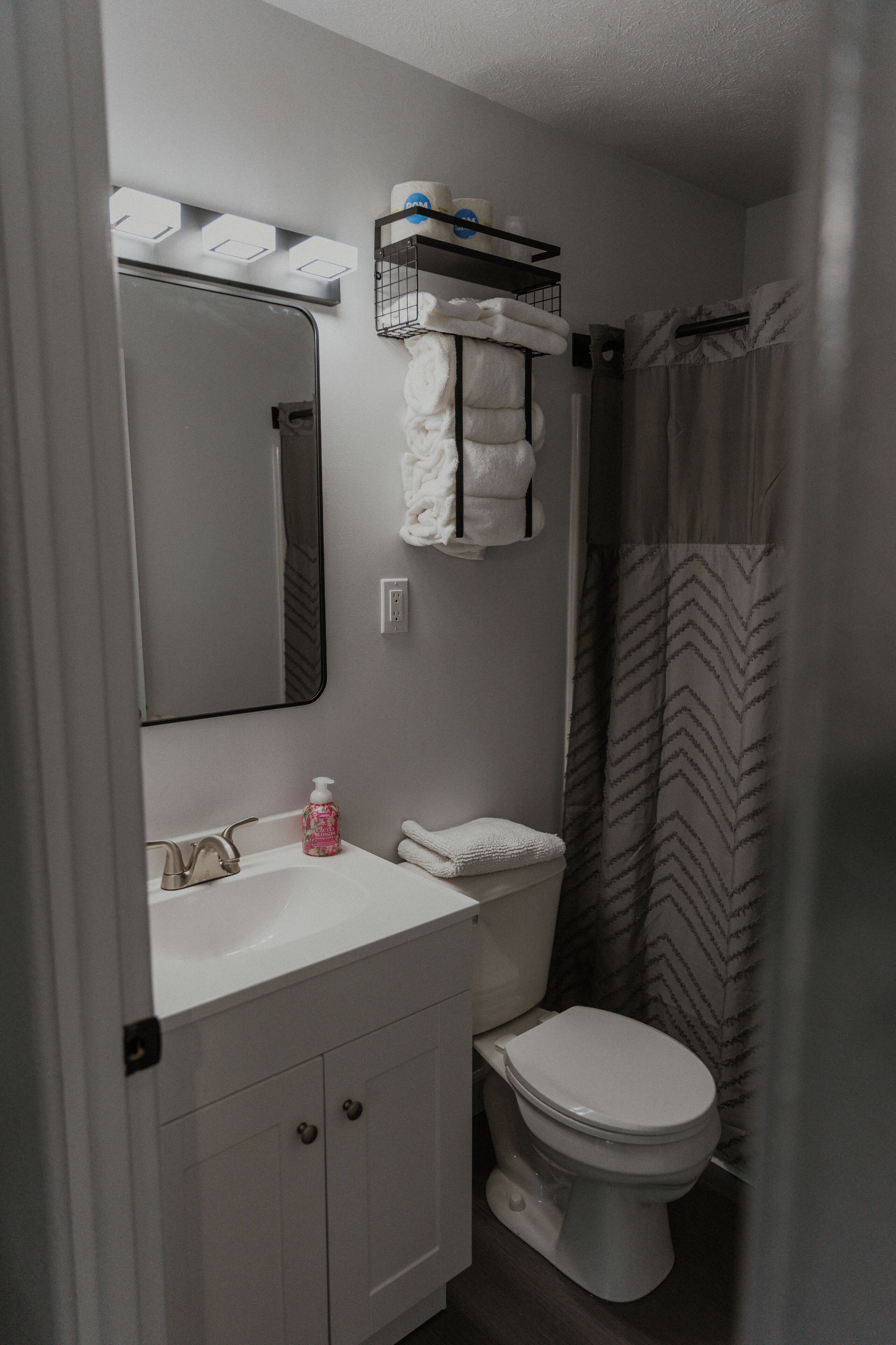 A bathroom with a sink, mirror, toilet, and shower curtain.