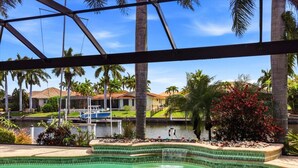 Una piscina con una fuente de agua cristalina, rodeada de palmeras y vistas a casas al fondo.