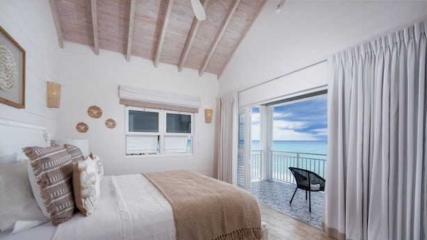A bedroom with a bed, a window, a balcony with a chair, and a view of the sea. - Sea Breeze House 5 Bedroom Villa (Prospect)