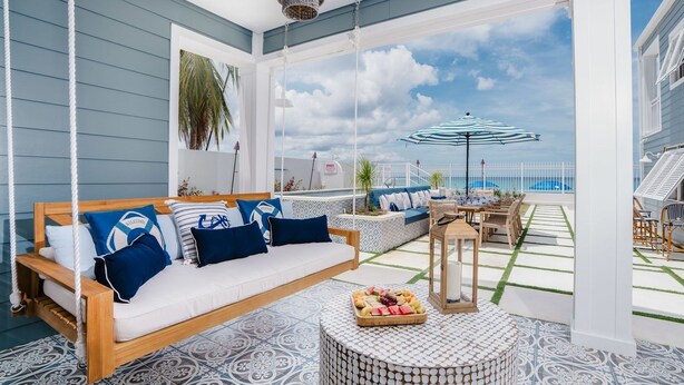 Un balcon avec un fauteuil suspendu, une table ronde sur laquelle est posé un panier de fruits, et une vue sur la mer.