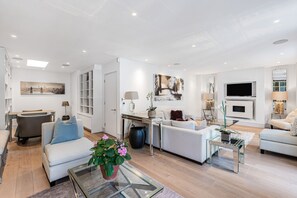 A modern living room with a sofa, coffee table, and TV. There is a dining area with a table and chairs. - Luxury Knightsbridge 4-bedroom House With Central AC (London)
