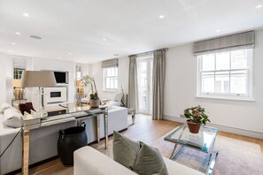 A modern living space with a sofa, coffee table, TV, and a dining area. - Luxury Knightsbridge 4-bedroom House With Central AC (London)