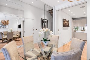 A modern interior with a glass dining table, cushioned chairs, and a vase of white orchids. - Luxury Knightsbridge 4-bedroom House With Central AC (London)
