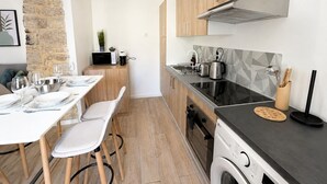 Moderni keittiö, jossa on pyykinpesukone, ruokailutila neljälle katetulla pöydällä sekä kiviseinä.