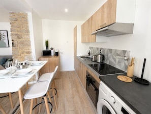 Une cuisine moderne équipée d’un lave-linge, un coin repas avec une table dressée pour quatre personnes, et un mur en pierre.