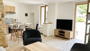 Moderni olohuone, jossa on ruokailutila, musta sohva, TV-taso ja kiviseinä.