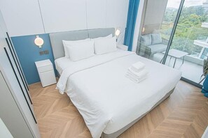Habitación de hotel moderna con una cama grande, una mesita de noche, una pequeña mesa y un balcón con vistas.
