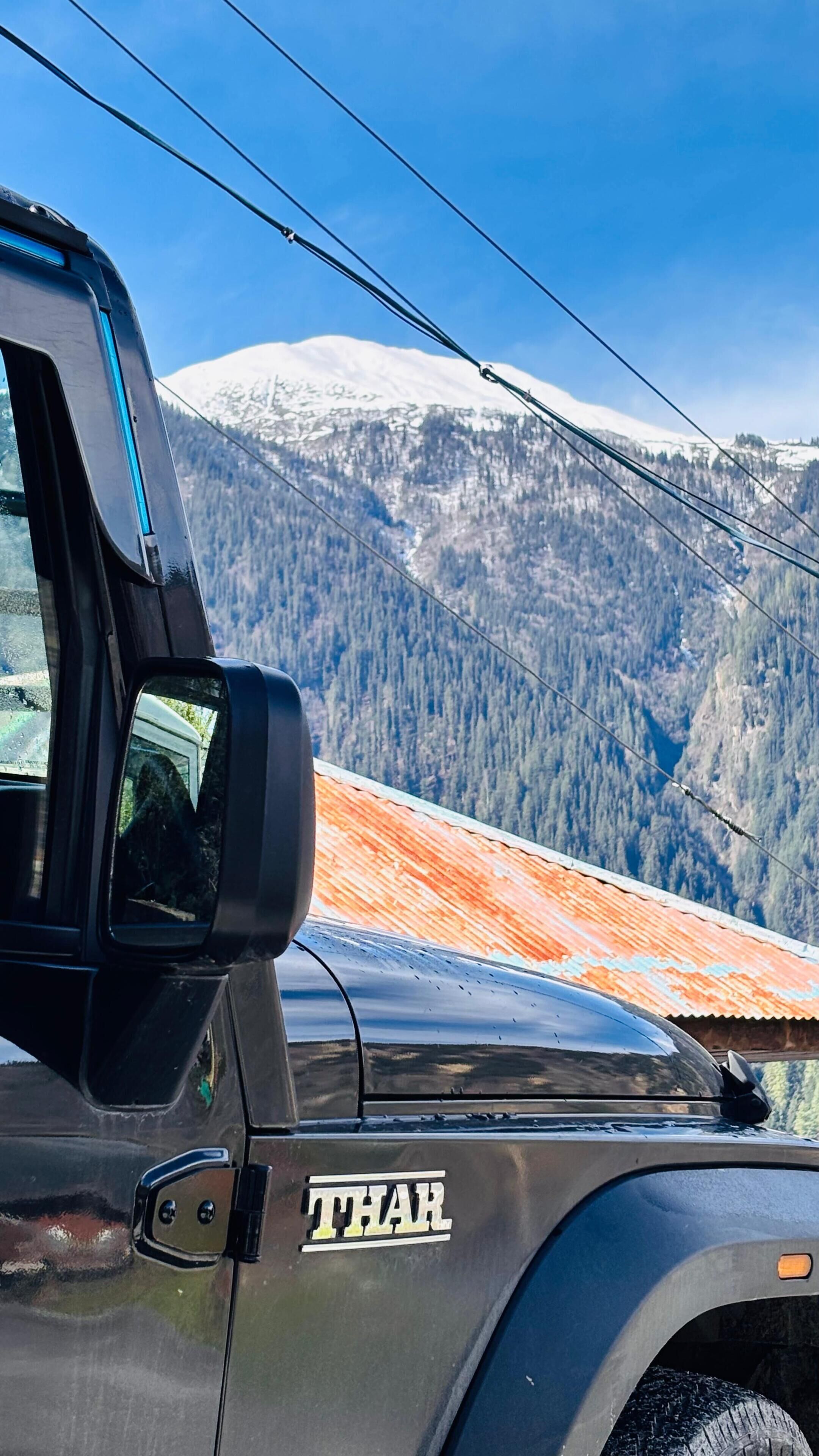 Um veículo THAR com espelho retrovisor, logotipo visível e paisagem montanhosa ao fundo.