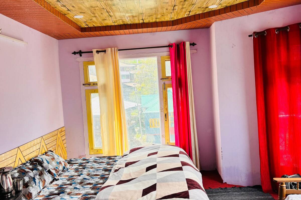 A bedroom with a bed, a window with curtains, a wooden ceiling, and a view of the outside.