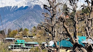 A mountainous landscape with snow-capped peaks in the background, a stone staircase, and buildings with green roofs. - Dolma homestay by Orko (Nichar)