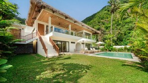 A two-story house with a thatched roof, a swimming pool, and a lush garden. - Villa Svara - 4BR Villa w/ Panoramic Ocean Views (Purwakerti)