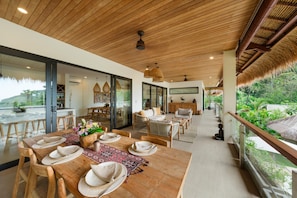A spacious dining area with a wooden table set for four, surrounded by wicker chairs and a patterned rug. - Angin Laut - Private Villa with Three Bedrooms (Purwakerti)