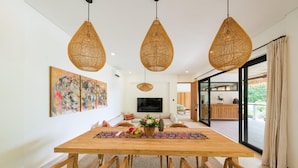 A dining area with a wooden table, woven chairs, and three hanging wicker pendant lights. - Angin Laut 3BR Exclusive Pool Villa w/ Ocean Views (Purwakerti)