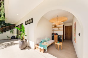 A modern living space with a sofa, a small table, a potted plant, and a staircase. - Angin Laut - Private Villa with Three Bedrooms (Purwakerti)