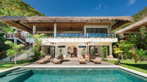A resort with a pool, lounge chairs, and a thatched-roof building. - Angin Laut 3BR Exclusive Pool Villa w/ Ocean Views (Purwakerti)