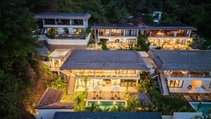 A multi-story resort with a pool, thatched-roof structures, and lush greenery. - Angin Laut 3BR Exclusive Pool Villa w/ Ocean Views (Purwakerti)