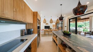 A modern kitchen with wooden cabinetry, a marble countertop, and pendant lighting. - Angin Laut 3BR Exclusive Pool Villa w/ Ocean Views (Purwakerti)