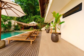 A poolside area with lounge chairs, umbrellas, and potted plants.