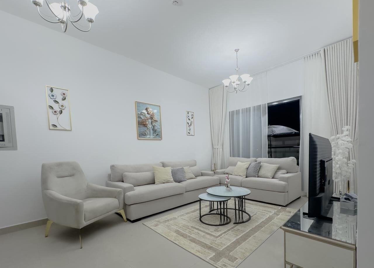 A modern living room with a sofa set, a round coffee table, a TV, and a chandelier.