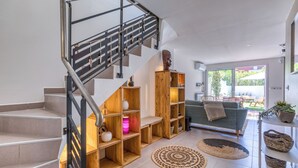 A modern interior with a staircase, wooden shelving, a sofa, and a dining area.
