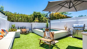 A backyard with artificial grass, a barbecue grill, a pool, and outdoor seating.