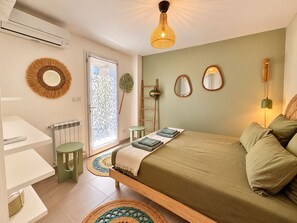 A bedroom with a bed, bedside tables, a radiator, a window with a frosted glass door, and a hanging light fixture. - Villa Cocoon—Private Pool—Near the Ocean & Montpellier (Mauguio)