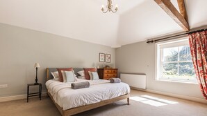 Ein Schlafzimmer mit Bett, Nachttisch, Kommode, Heizkörper und einem Fenster mit Vorhängen.