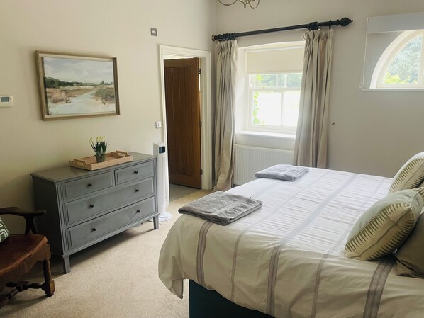 A bedroom with a bed, a dresser, a window with curtains, a radiator, and a painting on the wall.