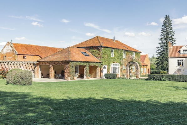 A large, multi-story house with a brick exterior, a tiled roof, and a well-maintained lawn.