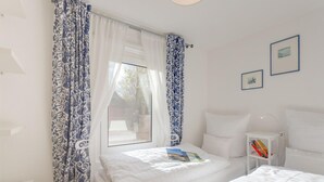 A bedroom with two beds, a bedside table, a lamp, and a window with curtains. - Ferienhaus am Achterwasser in Lutow (Luetow)