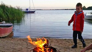 A beach scene with a campfire, a boat, and a child in a red jacket. - Ferienhaus am Achterwasser in Lutow (Luetow)