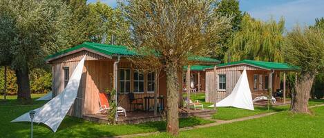 A row of wooden cabins with green roofs, surrounded by trees and grass.