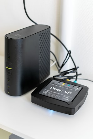 A black electronic device with a screen labeled 'Box 4K' and a power cord plugged in. - Charming T2 near RER and Stade de France (Saint-Denis)