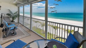 Ein Balkon mit Blick auf einen Strand, ein Stuhl, ein Tisch und ein hängender Vogel-Schmuck.