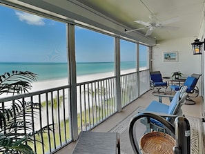 Un balcon avec vue sur la plage, un ventilateur de plafond et des chaises bleues.