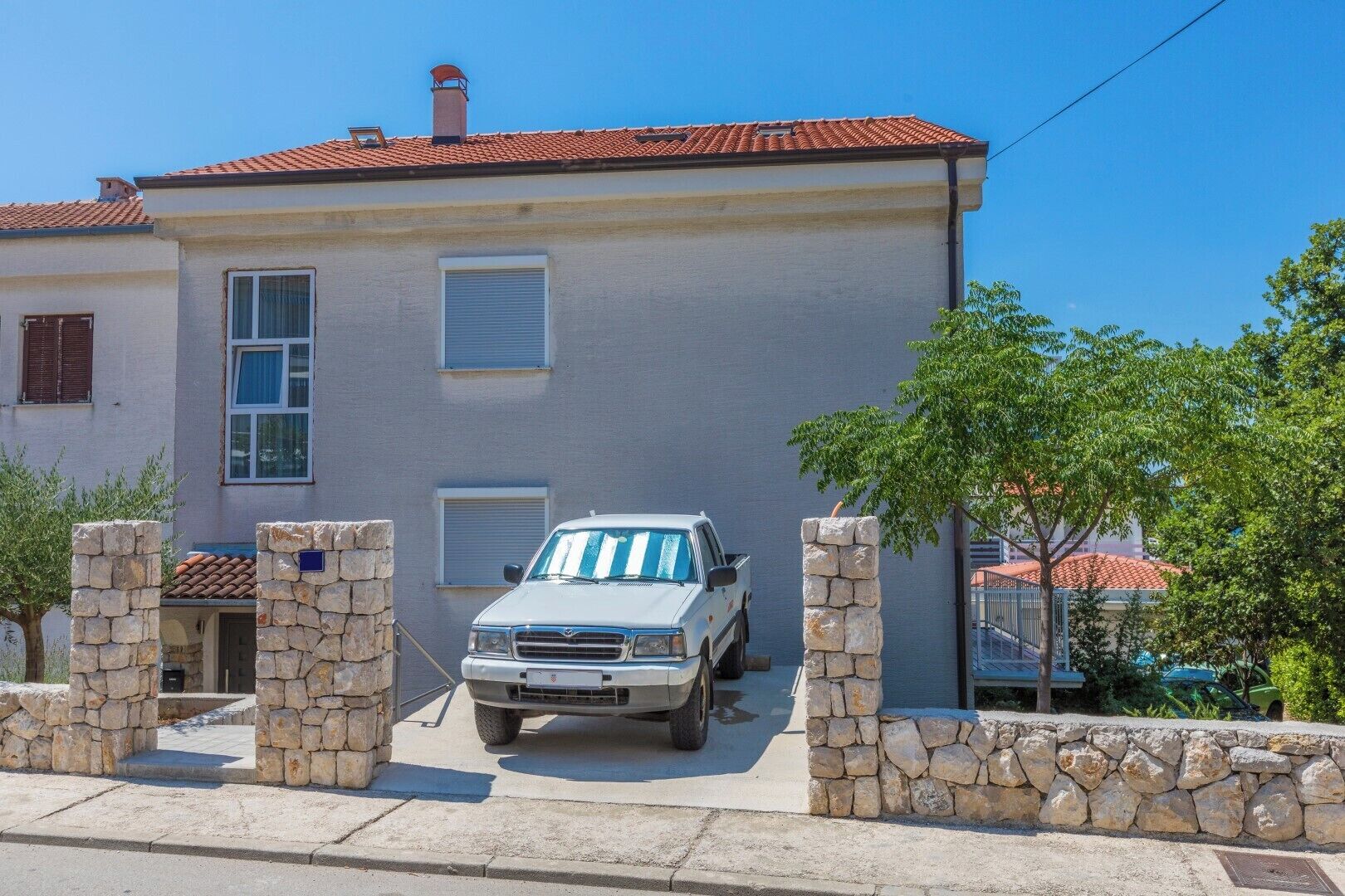 A two-story building with a stone wall entrance, a parked truck, and a clear blue sky.