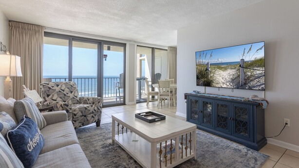 Un salon comprenant un canapé, un fauteuil, une table basse et un téléviseur. Il y a un balcon avec vue sur la plage.