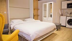 Ein Schlafzimmer mit Bett, Stuhl, Kleiderschrank, Spiegel und Waschmaschine.
