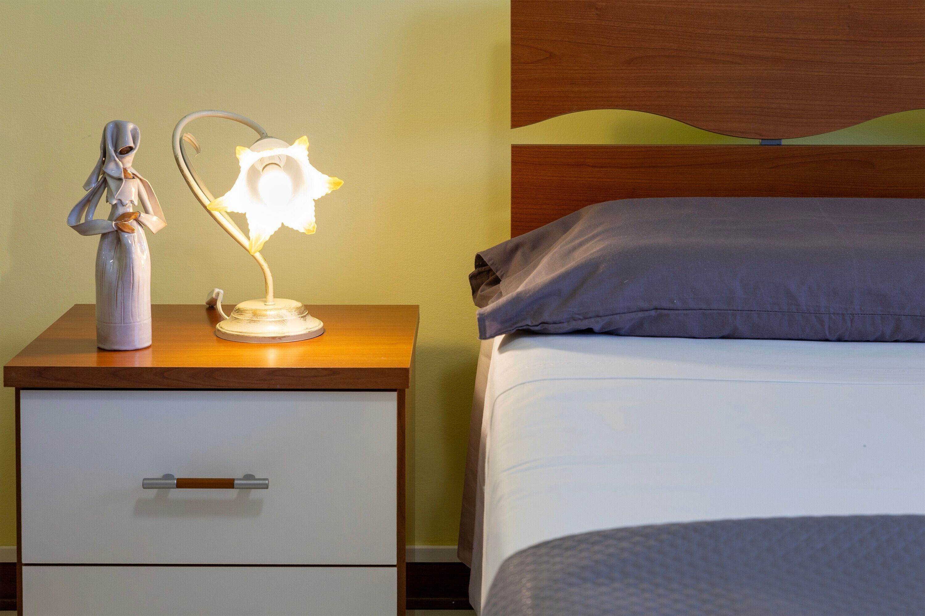 Un lit avec un oreiller, une table de chevet avec une lampe et un tiroir.