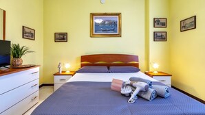 Hotellihuone, jossa on sänky, kaksi yöpöytää valaisimineen, televisio, lipasto ja seinällä olevia tauluja.