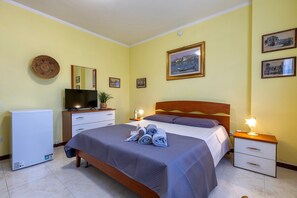 A bedroom with a bed, bedside tables, a television, and a refrigerator.