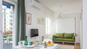 A modern living room with a green sofa, a dining table with a vase and fruit, and a TV on the wall. - Lambrate Design District - Apartment a stone's throw from the subway (Milano)