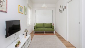 A modern living room with a flat-screen TV, green sofa, white walls, and a door. - Lambrate Design District - Apartment a stone's throw from the subway (Milano)